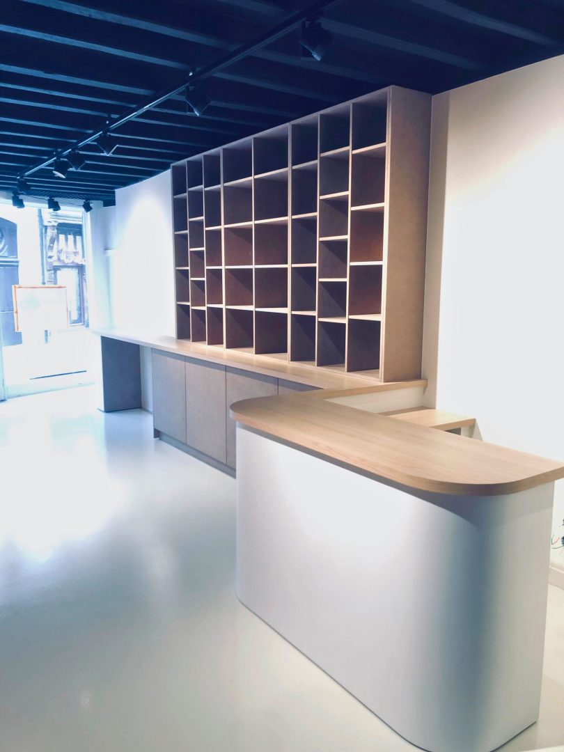 Fabrication et pose d'un ensemble de mobilier de présentation pour l'espace de vente d'une boutique avec une banque d'accueil cintrée